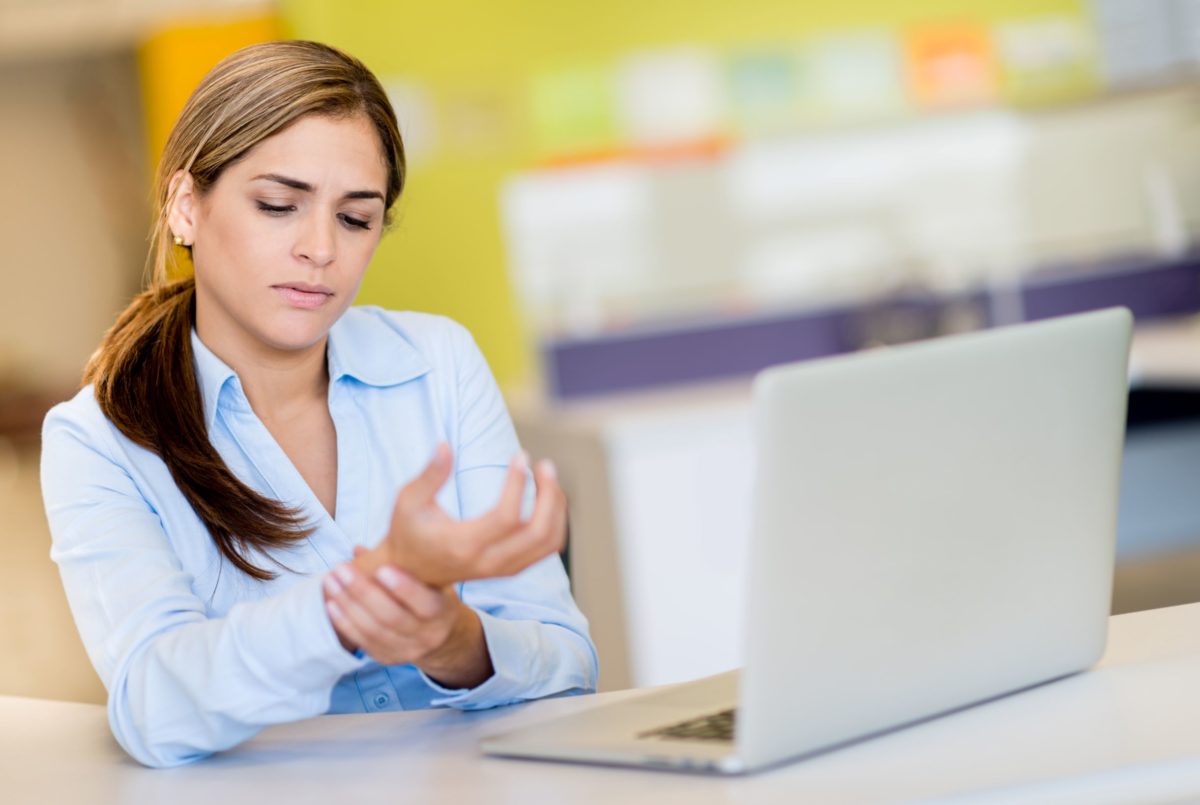 Various factors place some people at risk of getting carpal tunnel syndrome (CTS). Women, for example, are more likely to get CTS than men are. In this image, a woman working at a computer is holding her wrist in pain.