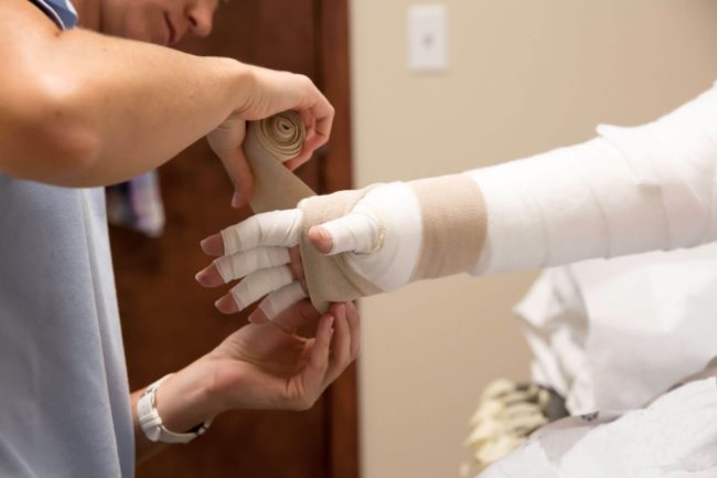 Conditions such as lymphedema show signs in the hands and arms. In this image, a medical care practitioner wraps a patient's hand and wrist as a form of lymphedema therapy.