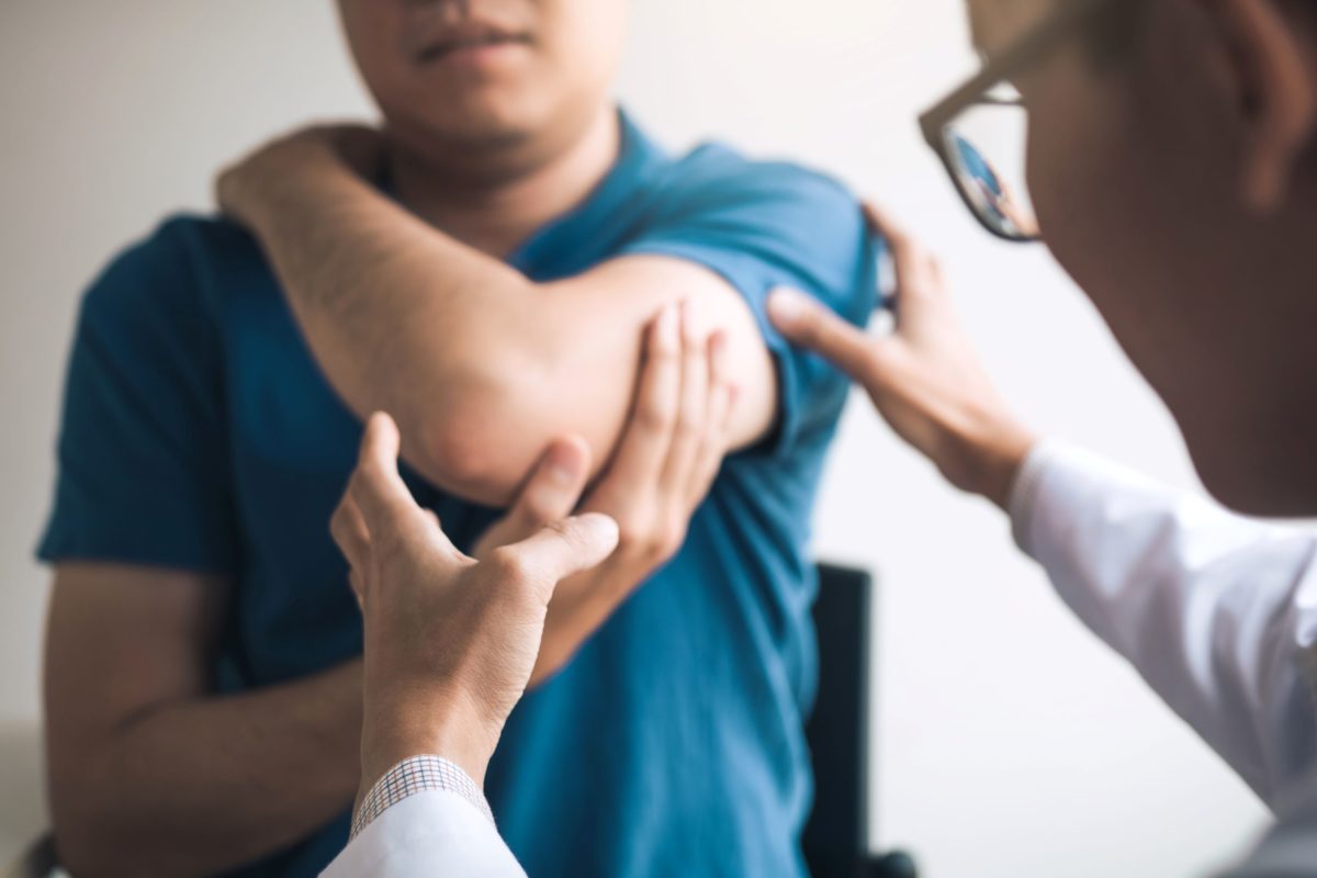 A doctor examines a patient's elbow in this image. Common conditions that may require elbow surgery are tennis elbow, golfer's elbow, cubital tunnel syndrome, fractures, and olecranon bursitis.