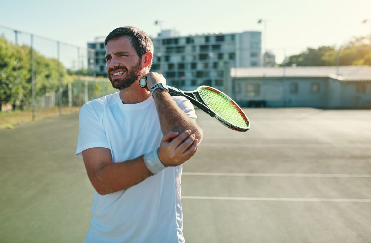 There are a few differences between tennis elbow and golfer's elbow. In this image, a man holding a racquet on a tennis court holds his elbow in pain.