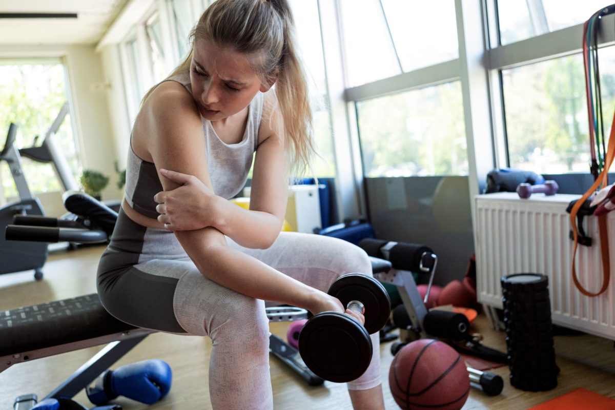 A woman lifting weights at the gym has a charley horse in her arm.